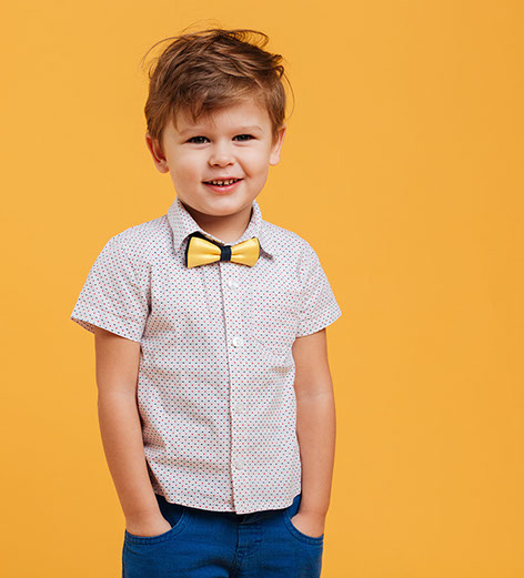 Image of happy little boy child standing isolated over yellow background. Looking aside.