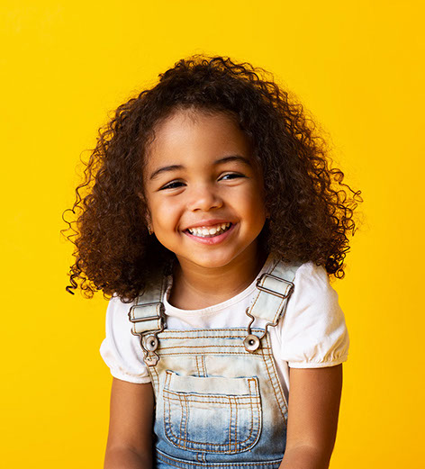 Happy african-american child girl smiling to camera over yellow background